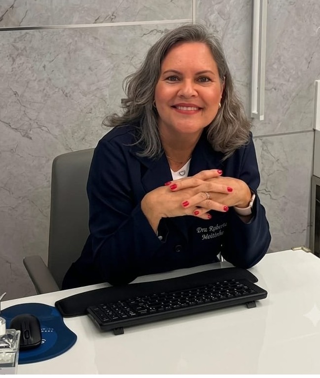 Dra. Roberta Leal sorridente em seu consultório, atenta ao atendimento